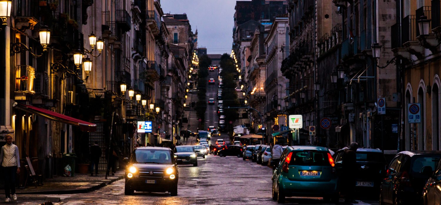 Night scene of Catania from a long street with a hill in the distance