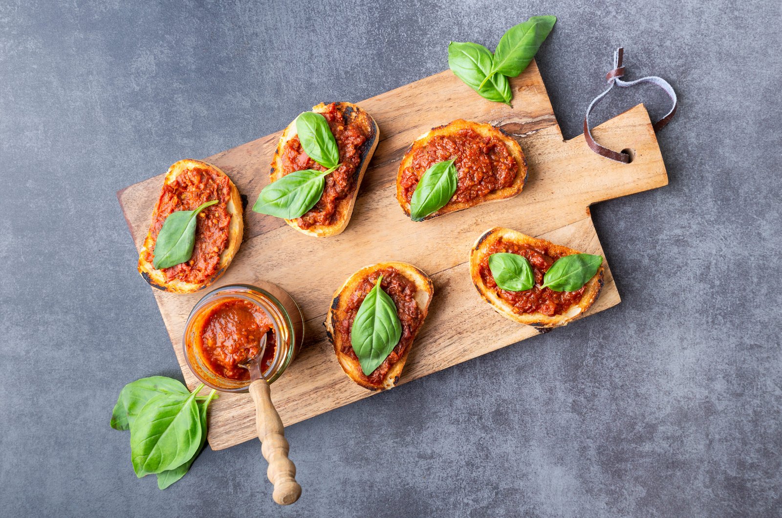 Tomatenpesto auf einem grauen Marmortisch und einem Holzschneidebrett